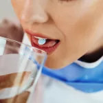 Close-up of a woman having a glass of water while taking a pill.