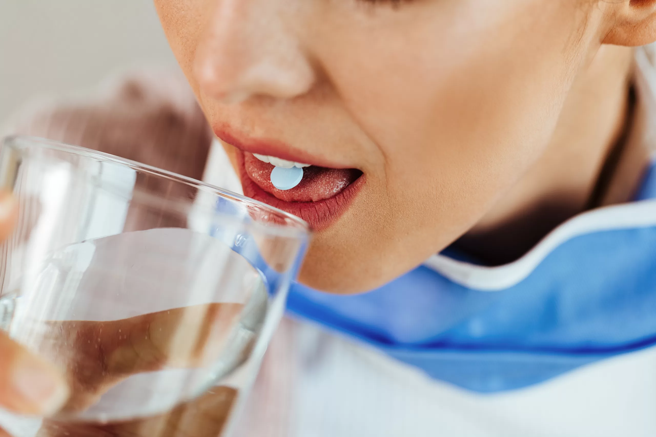 Close-up of a woman having a glass of water while taking a pill.