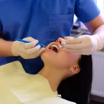 A dentist working on a young woman patient with dental tools at the Ridge Oral Surgery clinic.
