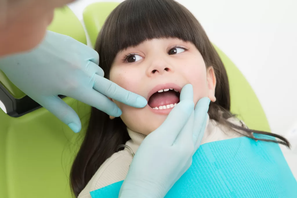 Close-up of a pediatric dentist examining a young girl’s teeth at Ridge Oral Surgery clinic.