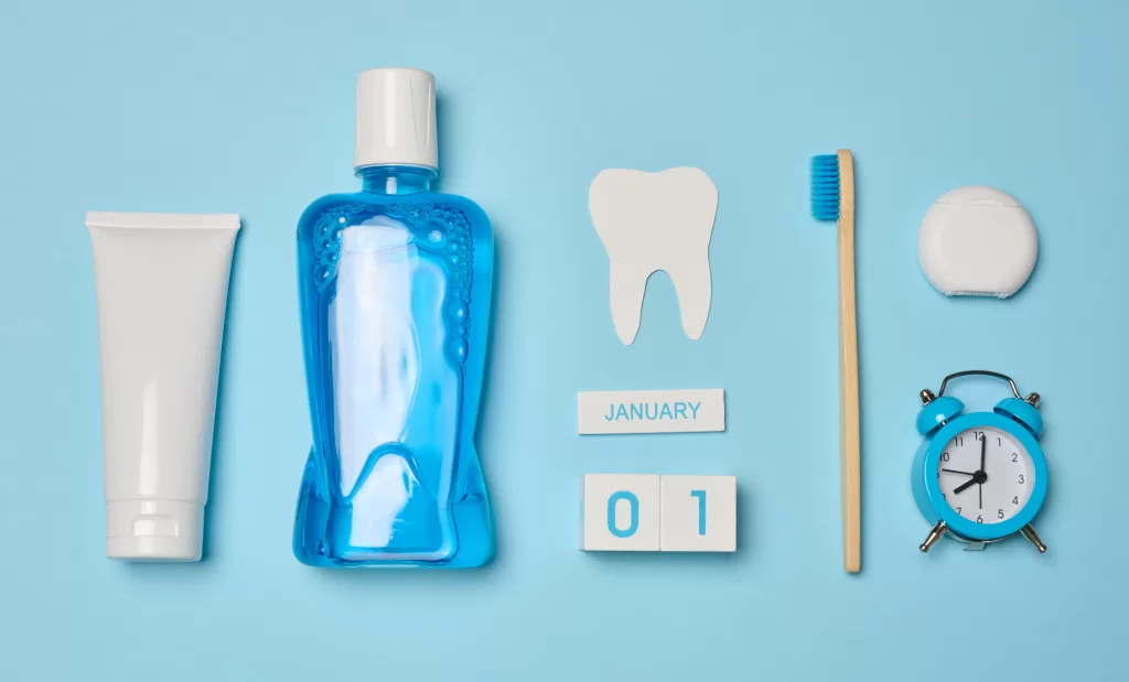 Mouthwash, toothpaste tube, dental floss, and an alarm clock on a blue background.
