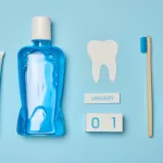 Mouthwash, toothpaste tube, dental floss, and an alarm clock on a blue background.