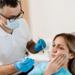 Patient holding jaw due to jaw pain, being checked by a dental professional at Ridge Oral Surgery.