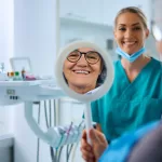Woman with implants looking in the mirror, surrounded by two dental professionals at Ridge Oral Surgery.