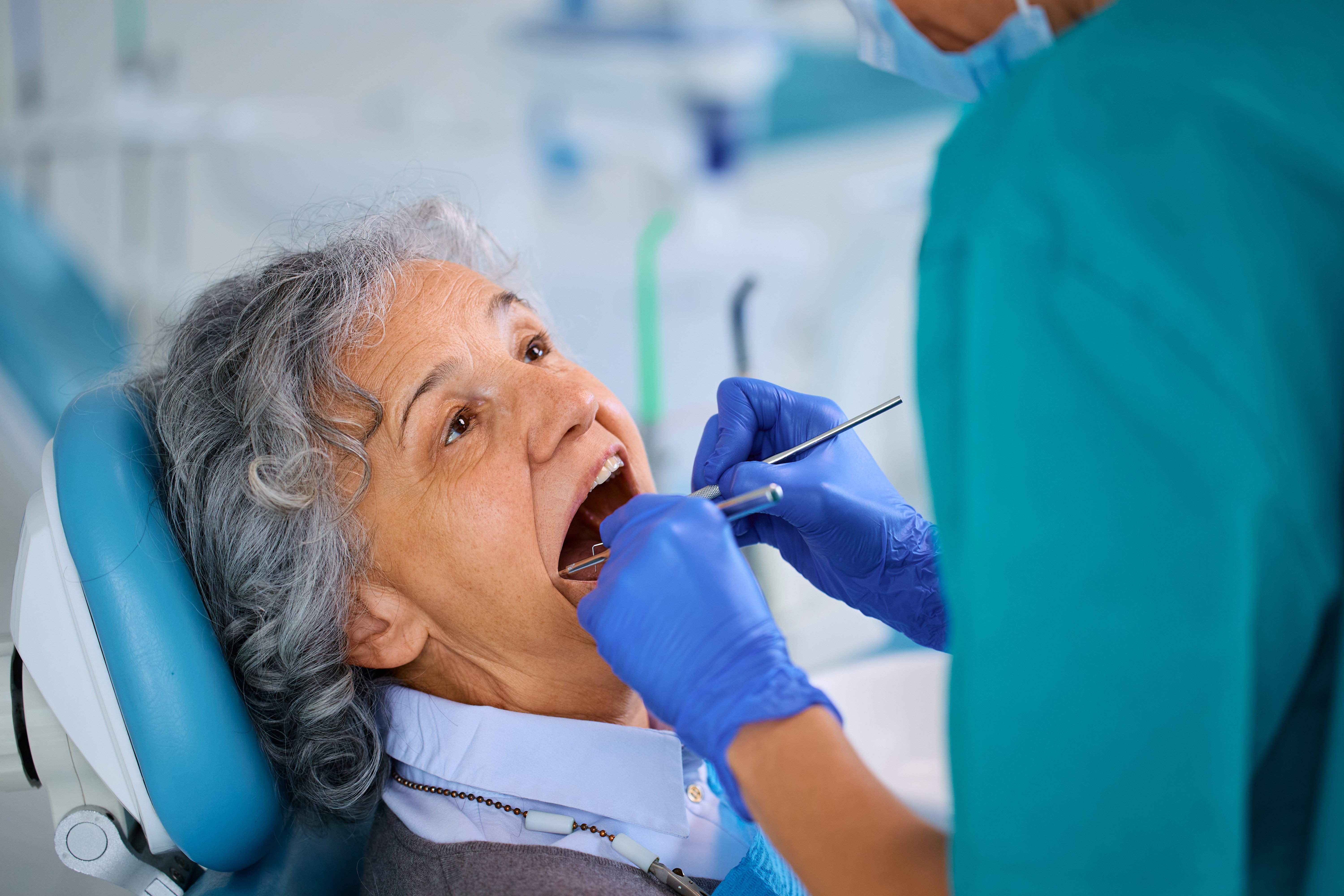 Elderly female patient receiving a dental examination for implants at an oral surgery clinic.