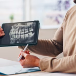 Dentist reviewing a patient's dental implant treatment plan and digital X-ray on a tablet during a consultation.