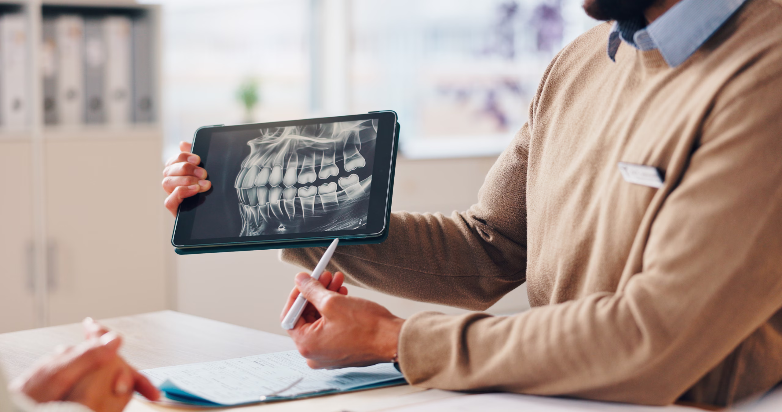 Dentist reviewing a patient's dental implant treatment plan and digital X-ray on a tablet during a consultation.