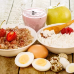 Recovery-friendly foods after wisdom teeth removal, including a yogurt smoothie, eggs, cottage cheese, fresh fruit, and oatmeal arranged on a table.