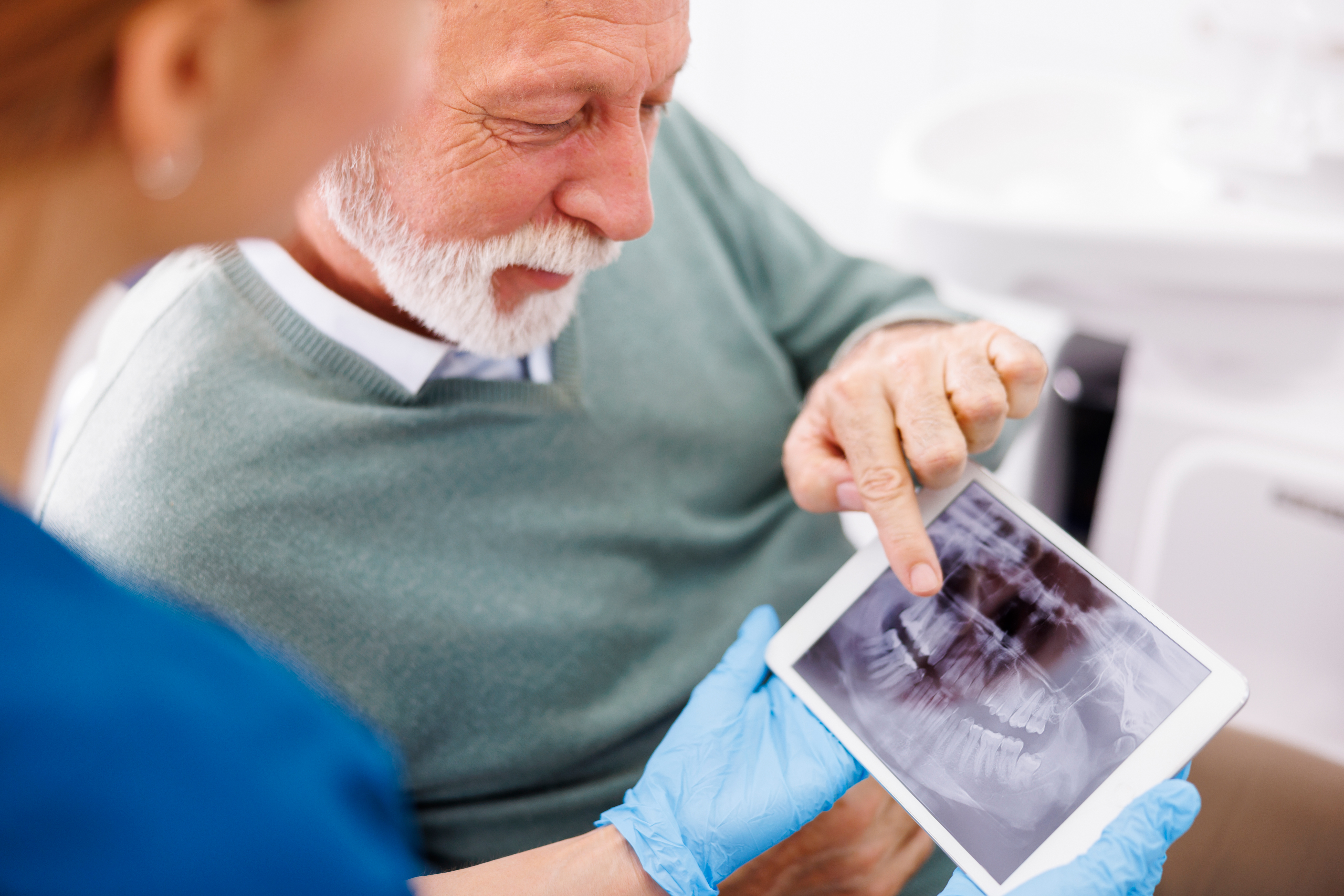 Patient reviewing a dental X-ray with an oral surgeon during a consultation about an older dental bridge and implant options.