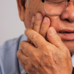 Older man experiencing jaw pain and holding his cheek near the temporomandibular joint.