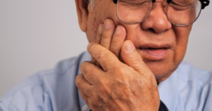 Older man experiencing jaw pain and holding his cheek near the temporomandibular joint.