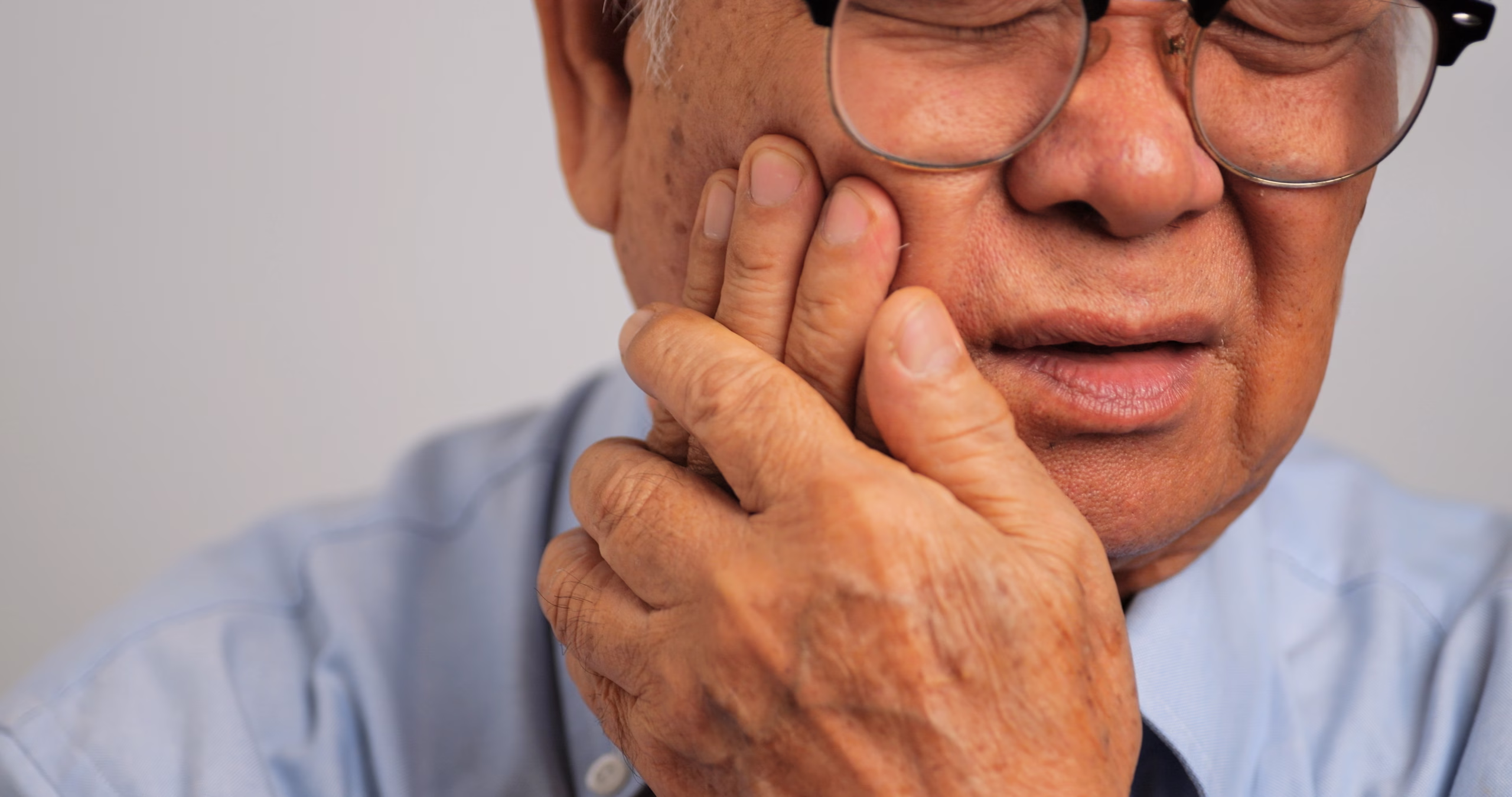 Older man experiencing jaw pain and holding his cheek near the temporomandibular joint.